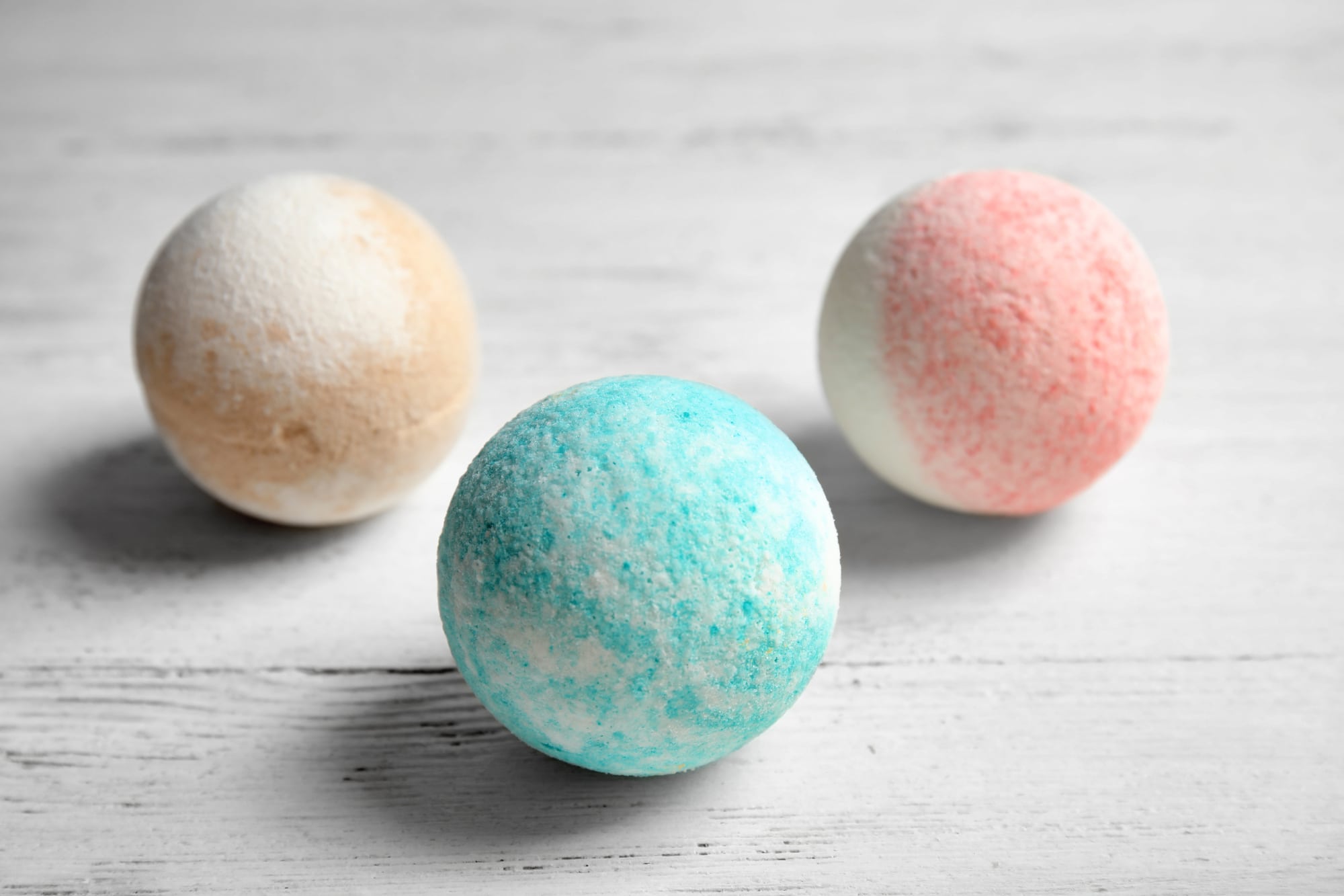 Three pastel colored bath bombs on a white wooden board